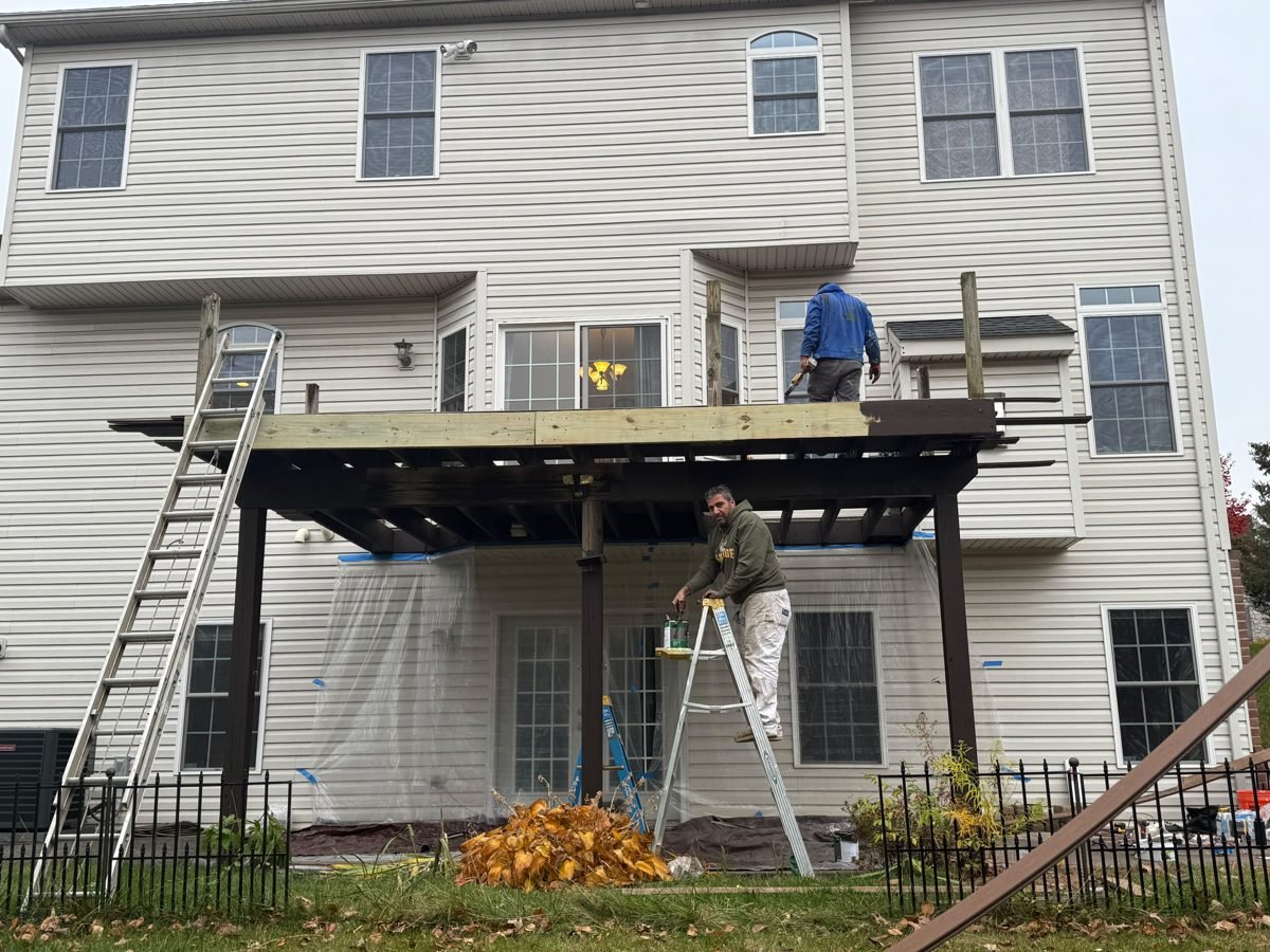 Crew framing a second-story deck: posts, beam and joists up, ladder against the house
