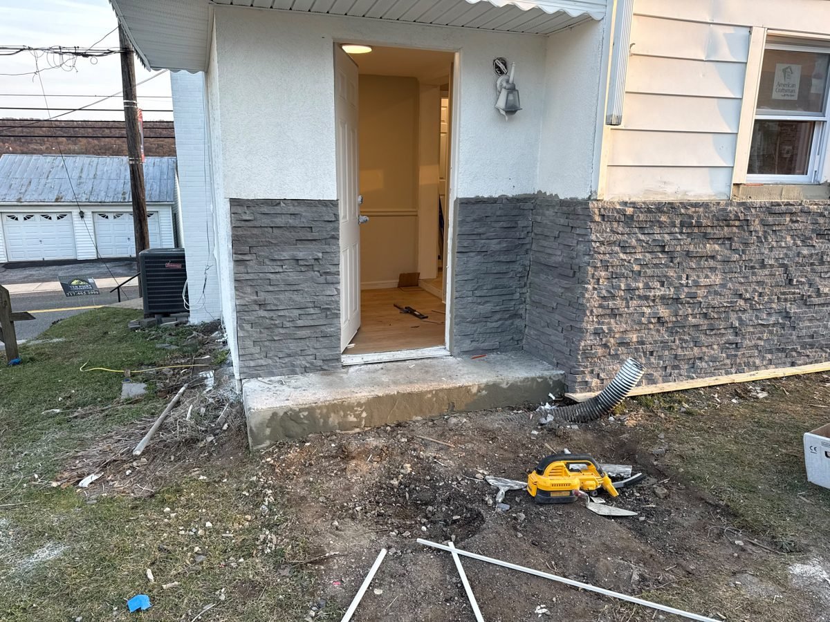 Rear entry of a house with new stone-veneer wainscot around a new door, work in progress
